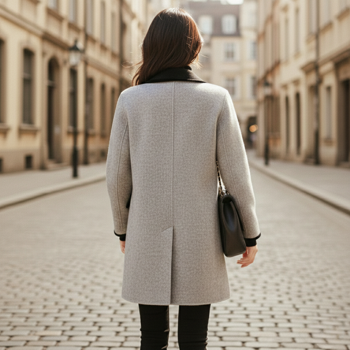 A woman wearing a knee-length double-breasted coat and black pants,  good for fall and winter outings.